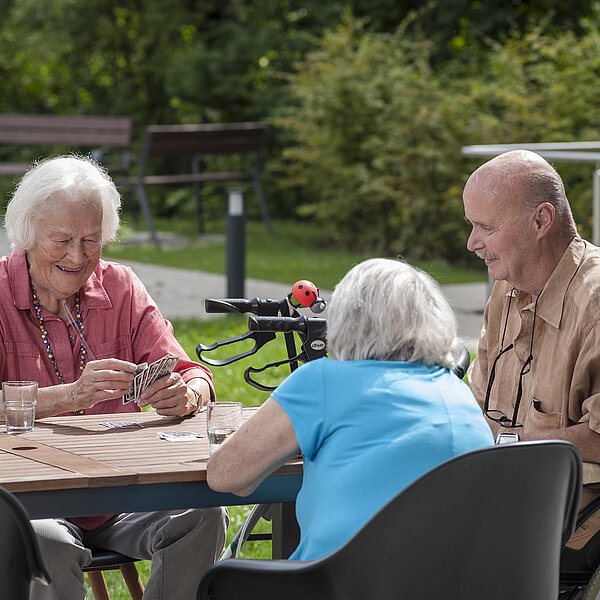 Drei ältere Personen spielen auf einer Terrasse Karten.